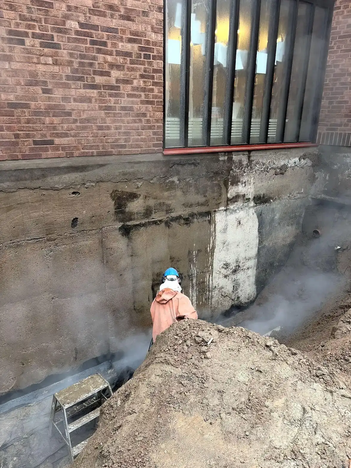 Vattenblästring av betonggrund vid schakt intill tegelbyggnad